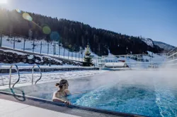 Frau entspannt in beheiztem Außenpool mit Blick auf verschneite Alpen