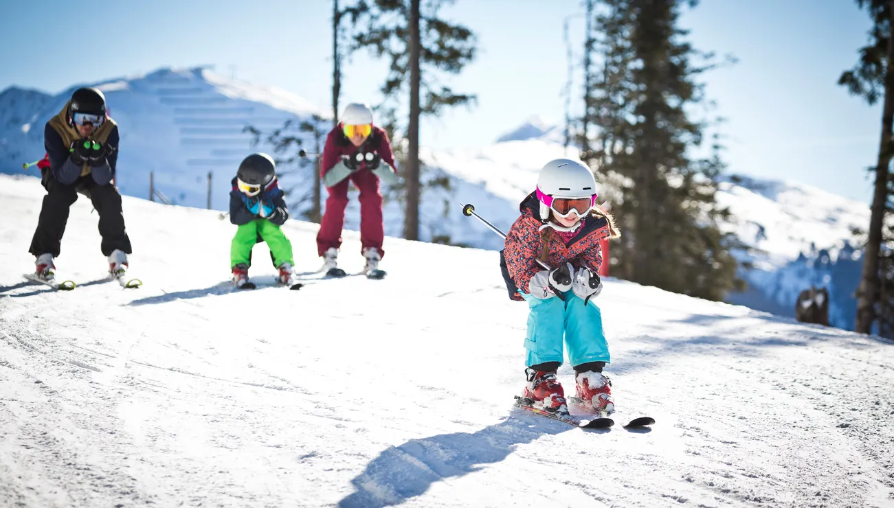 Kinder fahren in Formation einen sonnigen, verschneiten Berghang hinunter