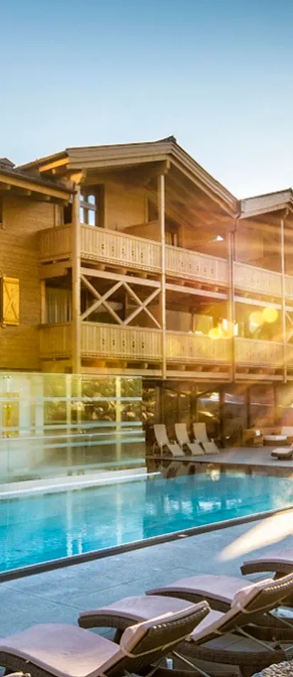 Luxury alpine resort with outdoor pool and sun loungers at sunrise