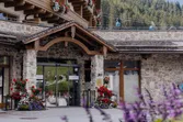 Entrance of alpine hotel with wooden balconies, flowers, and cable cars in the background