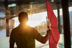 Man holding red spa flag by indoor pool with sunset shining through window