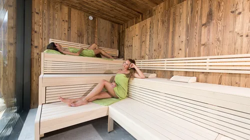 Frauen entspannen auf Holzbänken in moderner Sauna mit Handtuchumhängen
