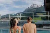 Couple in swimwear relaxing by rooftop pool with mountain view in summer