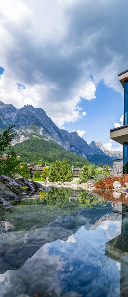 Modern mountain hotel with glass facade overlooking landscaped pond and alpine scenery