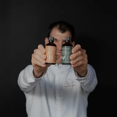 Man in white shirt holding two bottles of fermented Garum sauces against dark background