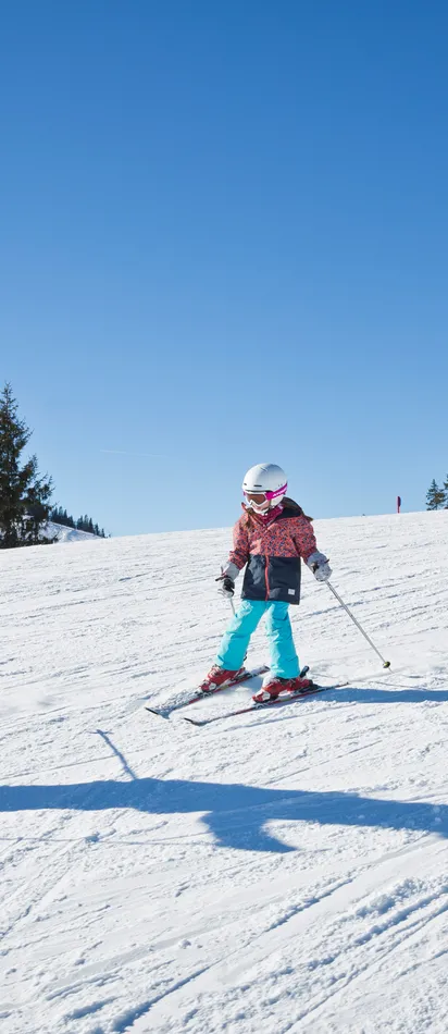 Familie fährt gemeinsam Ski auf sonniger Piste, Kinder lernen Skifahren