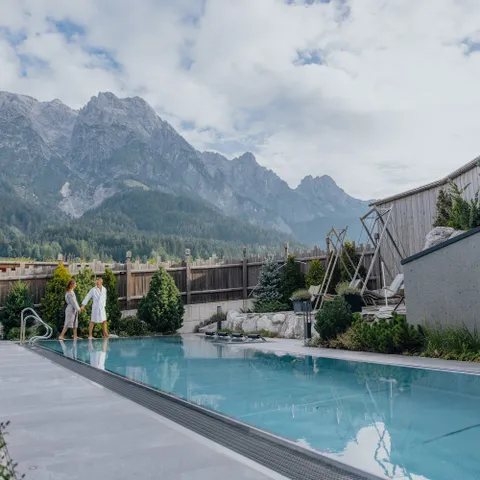 Paar spaziert am Außenpool mit Bergblick im luxuriösen Alpenresort