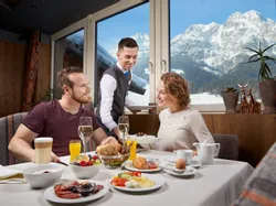Couple enjoying hotel breakfast with mountain view while server brings food