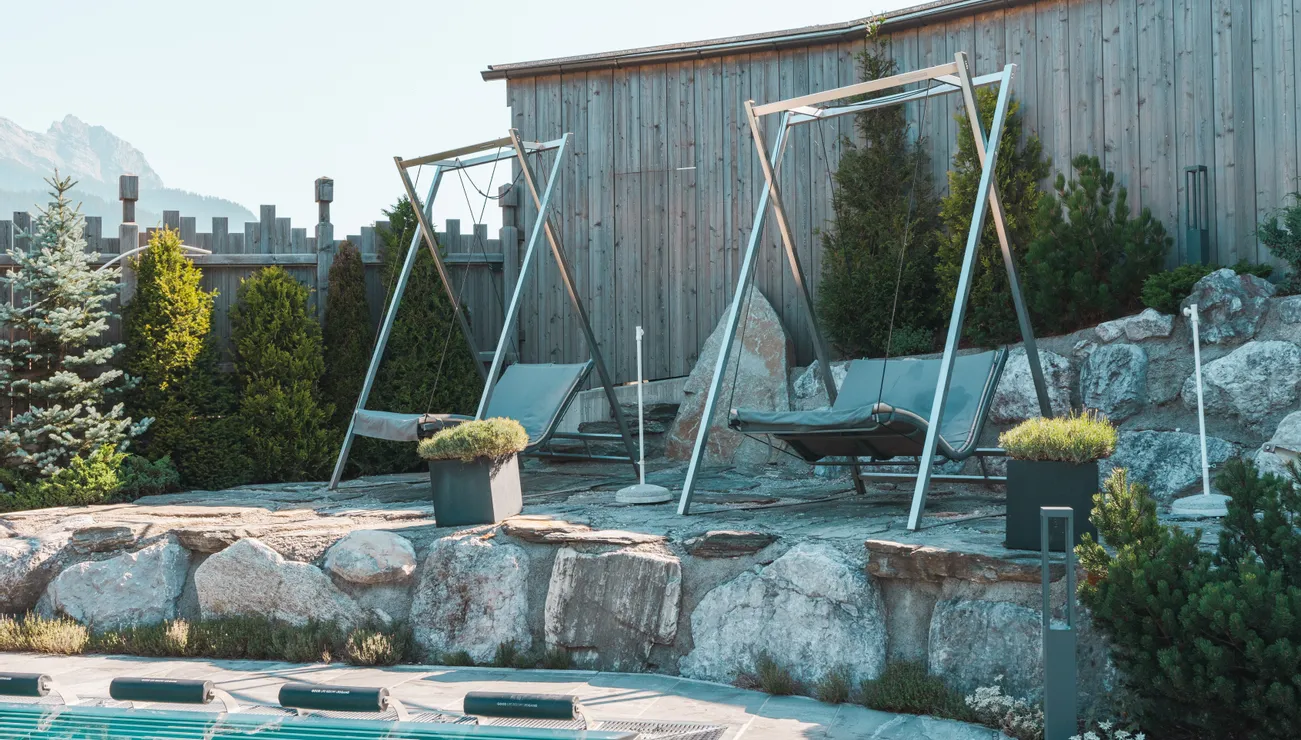 Modern outdoor lounge swings by a pool with wooden fence and mountain view