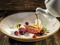 Gourmet Entenbrust mit Rotkohl, Kirschen und Sauce auf rustikalem Teller serviert