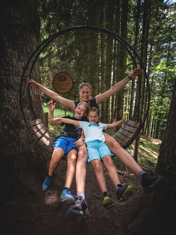 Happy family sitting on a circular wooden swing in a forest in Saalfelden Leogang